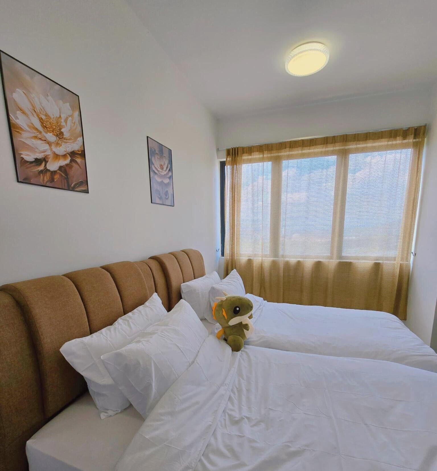 Ett hotellrum med två sängar, en brun sänggavel, vita sängkläder och ett fönster med gardiner.