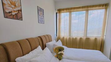 Ett hotellrum med två sängar, en brun sänggavel, vita sängkläder och ett fönster med gardiner.