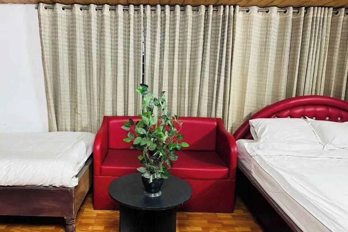 A hotel room with two beds, a red sofa, and a potted plant.