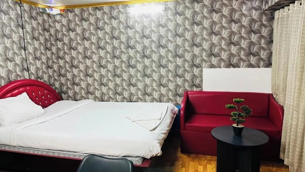 A room with a bed, a red sofa, a small table with a plant, and a textured wall.