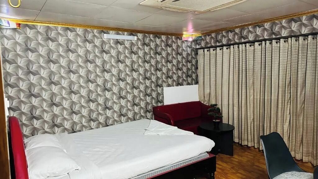 Una habitación de hotel con una cama, un sofá rojo, una mesita y una cortina.