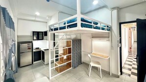 Une chambre compacte et moderne, équipée d’un lit superposé, d’un coin cuisine, d’une petite table et d’une chaise.