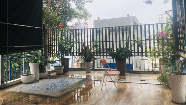 Un espace extérieur abrité, doté d’un sol carrelé, de plantes en pot et d’une chaise.