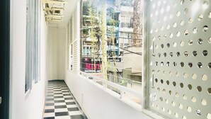 Un couloir au sol à carreaux, une fenêtre avec une grille métallique et une vue sur les bâtiments à l’extérieur.