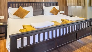 Ein ordentlich gemachtes Bett mit weißer und senffarbener Bettwäsche, ein Holz-Kopfbrett und ein Nachttisch mit Lampe.