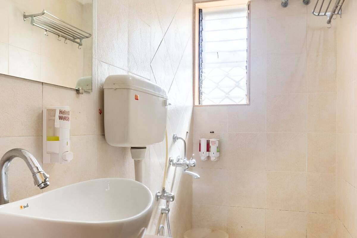 Een badkamer met een wit wastafel, toilet en douche. Er is een zeepdispenser en een handdoekhouder aan de muur.