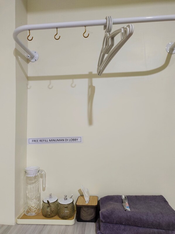 A bathroom with a towel rack, a sign indicating a free refill minimum, and a shelf with a glass jar, a wooden container, and a tissue box.