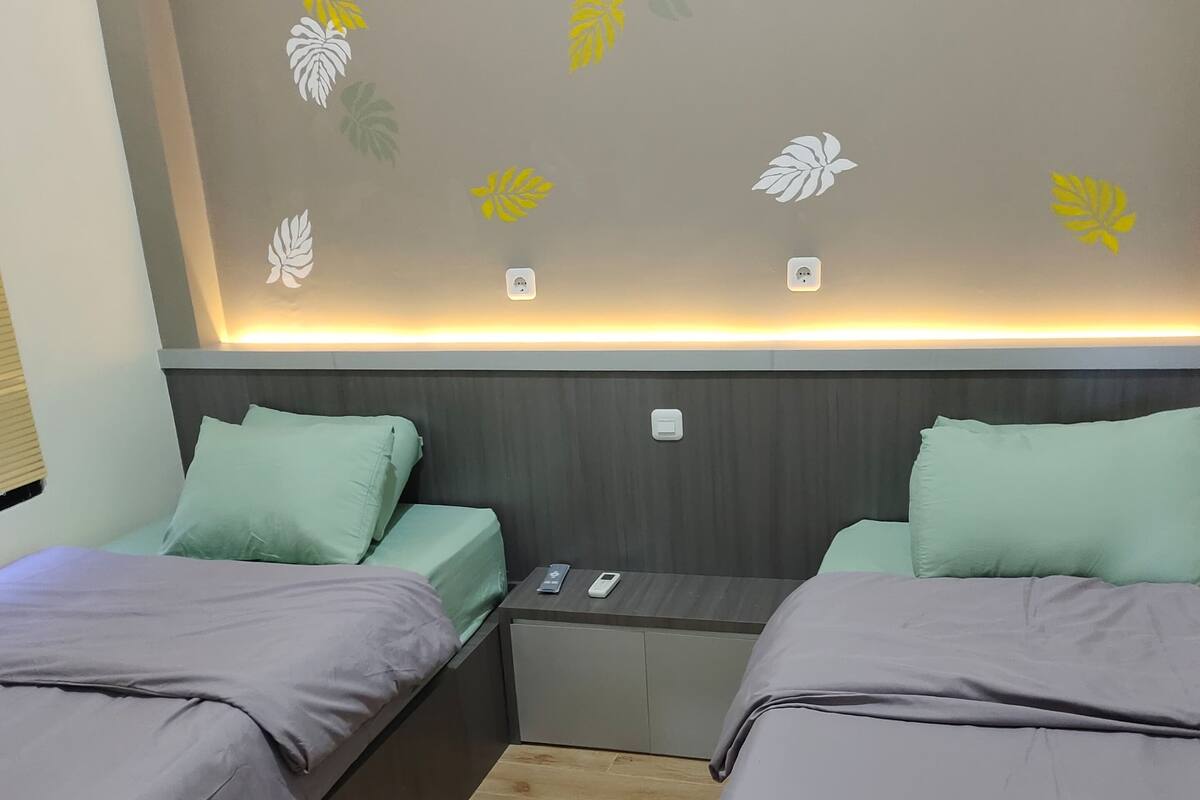 A hotel room with two beds, a wooden floor, and a wall with leaf decals.