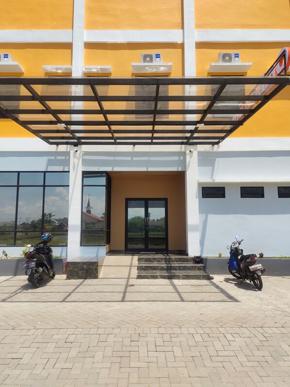 A building with a yellow and white facade, large windows, and a covered entrance area with two parked motorcycles.
