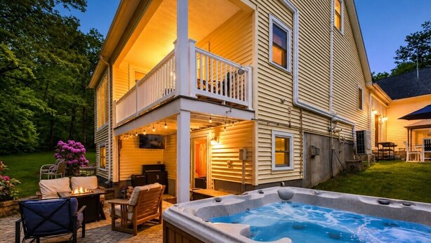 Una casa de dos pisos con un porche cubierto, mobiliario exterior y un jacuzzi.