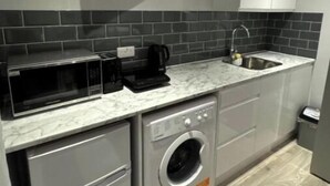 A compact kitchen with a microwave, coffee maker, and washing machine. - Cozy Cabin (Cricklewood)