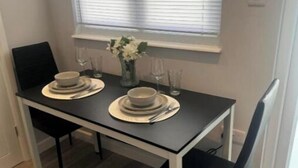 A dining table set with plates, bowls, and glasses, positioned near a window with blinds. - Cozy Cabin (Cricklewood)