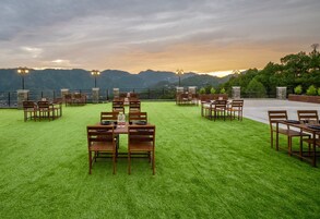 Un área de comedor al aire libre con mesas y sillas dispuestas sobre un césped, con vistas a un paisaje montañoso.