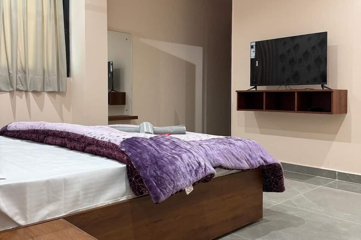 A modern bedroom with a bed, a ceiling fan, a TV mounted on the wall, and a wooden nightstand.