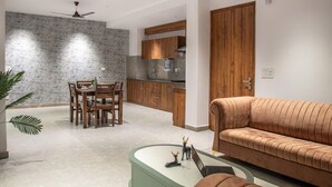 Una sala moderna con un sofá marrón, una mesa de comedor con sillas y una cocina al fondo.