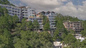 Un edificio residencial de varios pisos llamado Hill Crest, con arquitectura moderna, rodeado de abundante vegetación.