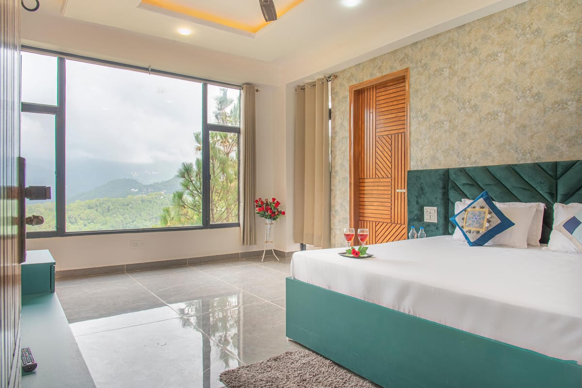 A bedroom with a large window, a bed with a green headboard, and a wooden door.