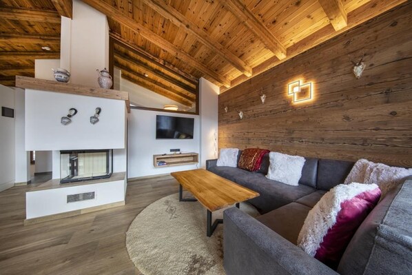 Una sala de estar moderna con techo de madera, un sofá gris, una mesa de centro de madera y una chimenea.
