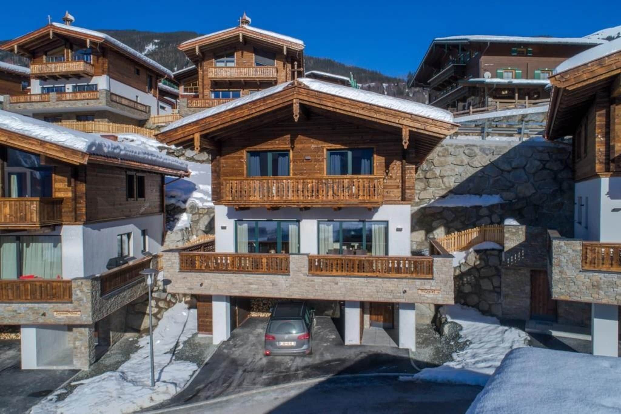 A multi-story wooden chalet with balconies, stone walls, and a car parked in front.