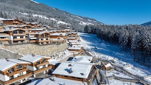 A snow-covered resort with wooden buildings, a ski slope, and a forested mountain backdrop. - Chalet near Ski Lift with Garden (Neukirchen)