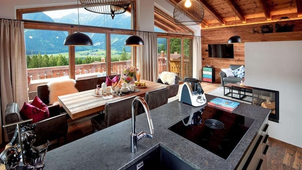 A modern kitchen with a large island, a dining area with a view, and a cozy seating area with a fireplace. - Chalet near Ski Lift with Garden (Neukirchen)