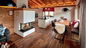 A modern interior with a wooden ceiling, a fireplace, a dining area, and a kitchen. - Chalet near Ski Lift with Garden (Neukirchen)