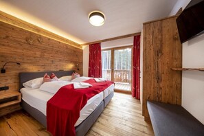Une chambre avec un mur en bois, un lit avec une literie rouge, un banc et un balcon avec des rideaux rouges.