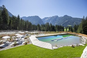 Une piscine dotée d’une terrasse en bois, entourée d’une clôture en bois, et offrant une vue sur les montagnes en arrière-plan.
