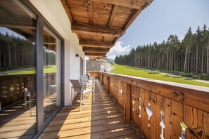 A wooden deck with glass doors, outdoor seating, and a view of a forested area. - Chalet in Neukirchen near Ski Lift (Neukirchen)