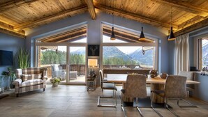 Une pièce spacieuse avec un plafond en bois, de grandes fenêtres et un coin repas comprenant des chaises et une table.