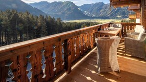 Une terrasse en bois, meublée de mobilier en osier, qui offre une vue sur un paysage montagneux.
