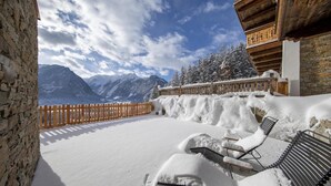 Zona exterior cubierta de nieve con sillones de descanso y valla de madera, con vistas a un paisaje montañoso.