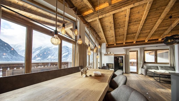 Interior de madera con ventanas amplias, techo de madera y una mesa larga.