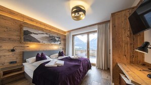 Habitación de hotel moderna con una cama grande, paredes de madera, vista a la montaña y un televisor de pantalla plana.