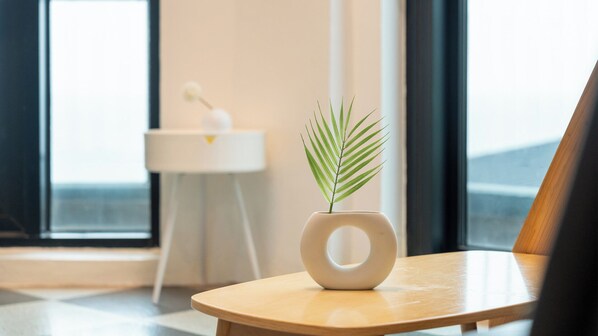 Une chambre moderne avec une table en bois, un vase blanc contenant une plante verte et une petite table d’appoint blanche agrémentée d’un objet décoratif.
