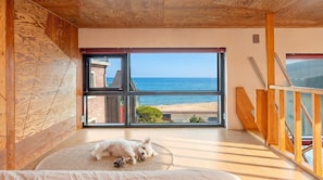 Ein Zimmer mit großem Fenster mit Blick auf einen Strand, ein Hund liegt auf einer Matte, und Holzvertäfelung an den Wänden.