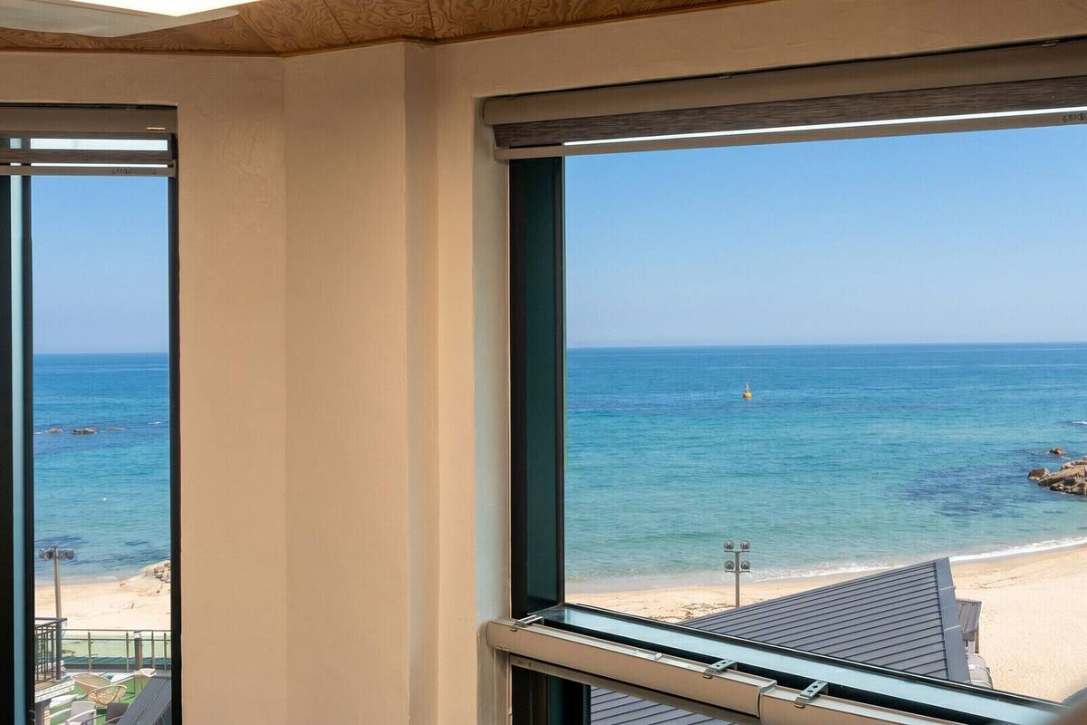 A room with large windows overlooking a beach, a view of the sea, and a sandy shore.