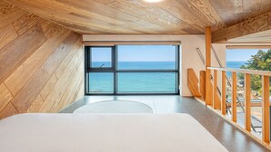 A bedroom with a large window overlooking the sea, wooden flooring, and a balcony with a railing. - Capella Oceanview Spa Resort Goseong (Goseong)
