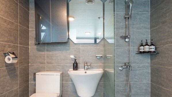 Un baño moderno con inodoro, lavamanos, ducha y espejo.