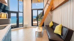 A modern living room with a view of the sea, a wooden slat ceiling, a black leather sofa with yellow cushions, and a small table with a vase. - Capella Oceanview Spa Resort Goseong (Goseong)