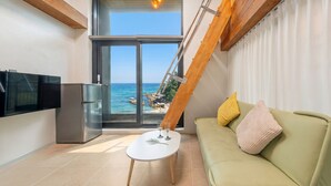 A modern living room with a sofa, a small table, a TV, and a large window offering a view of the sea. - Capella Oceanview Spa Resort Goseong (Goseong)