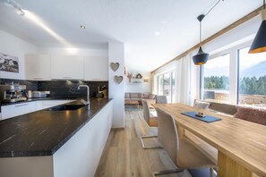 A modern kitchen with a black countertop, white cabinets, and a dining area with a wooden table and chairs. - Stylish Chalet by Ski Slopes (Neukirchen)