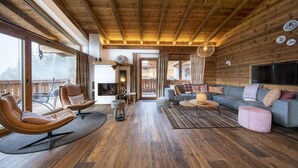 A spacious living room with a wooden ceiling, a grey sofa, leather armchairs, and a television.