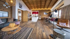 A spacious living area with a wooden ceiling, a sofa, a coffee table, and a dining area with chairs.