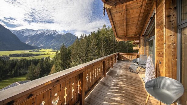 A wooden deck with a view of mountains and a forest.
