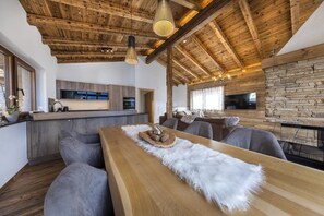 Un intérieur moderne avec un plafond en bois, un mur en pierre, un coin repas agrémenté d’un plaid en fourrure et une cuisine équipée d’appareils électroménagers intégrés.