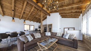 Ein großzügiger Wohnraum mit einer breiten Eckcouch, Holzboden und sichtbaren Holzbalken an der Decke.