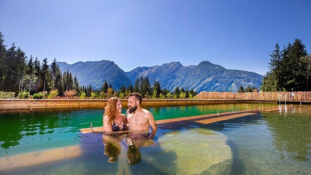 A couple in a clear pool with a mountain backdrop.
