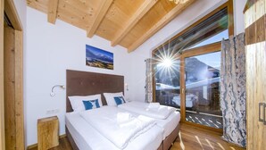 A bedroom with a large bed, wooden ceiling beams, a nightstand, and a view through a glass door.
