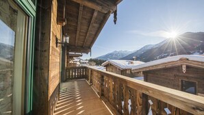 A wooden balcony with a view of snow-covered mountains and a bright sun.